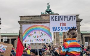 Eine Kundgebung vor dem Brandenburger Tor in Berlin. Auf den Schildern der Demoteilnehmenden, z.B. von einem Kind auf den Schultern eines Erwachsenen steht "Kein Platz für Rassismus"