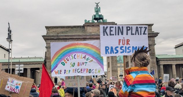 Eine Kundgebung vor dem Brandenburger Tor in Berlin. Auf den Schildern der Demoteilnehmenden, z.B. von einem Kind auf den Schultern eines Erwachsenen steht "Kein Platz für Rassismus"